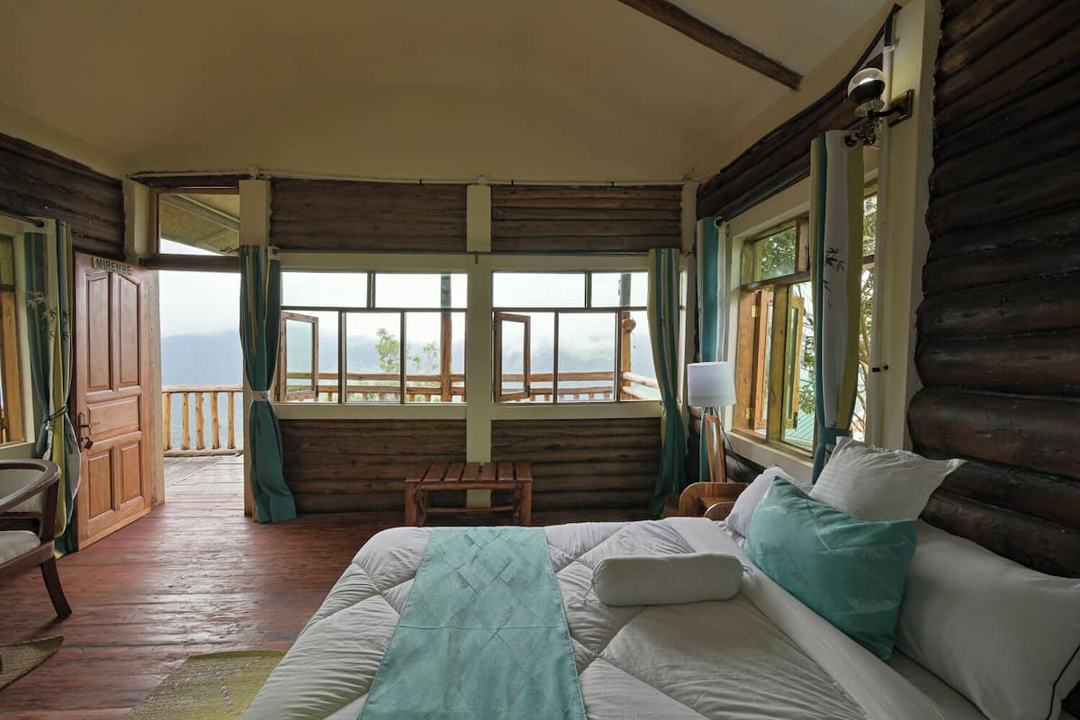 Ein gemütliches Blockhaus-Zimmer mit einem Bett, einer hölzernen Bank und Bergblick durch große Fenster.