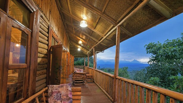 A wooden cabin with a covered porch, wooden railings, and a view of the mountains. - Orugano Bwindi Lodge (Nkuringo)