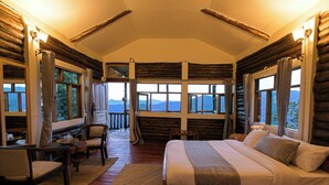 A log cabin bedroom with a bed, a desk, and chairs. - Orugano Bwindi Lodge (Nkuringo)