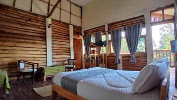 Una habitación tipo cabaña de madera con cama, sillas, una mesita y una ventana con cortinas.