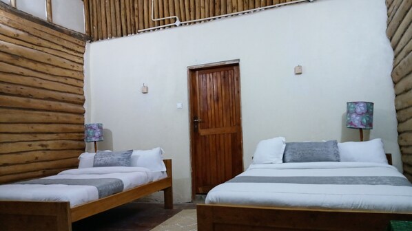 A room with two wooden beds, a wooden slatted ceiling, a wooden door, and a small wall-mounted light fixture.