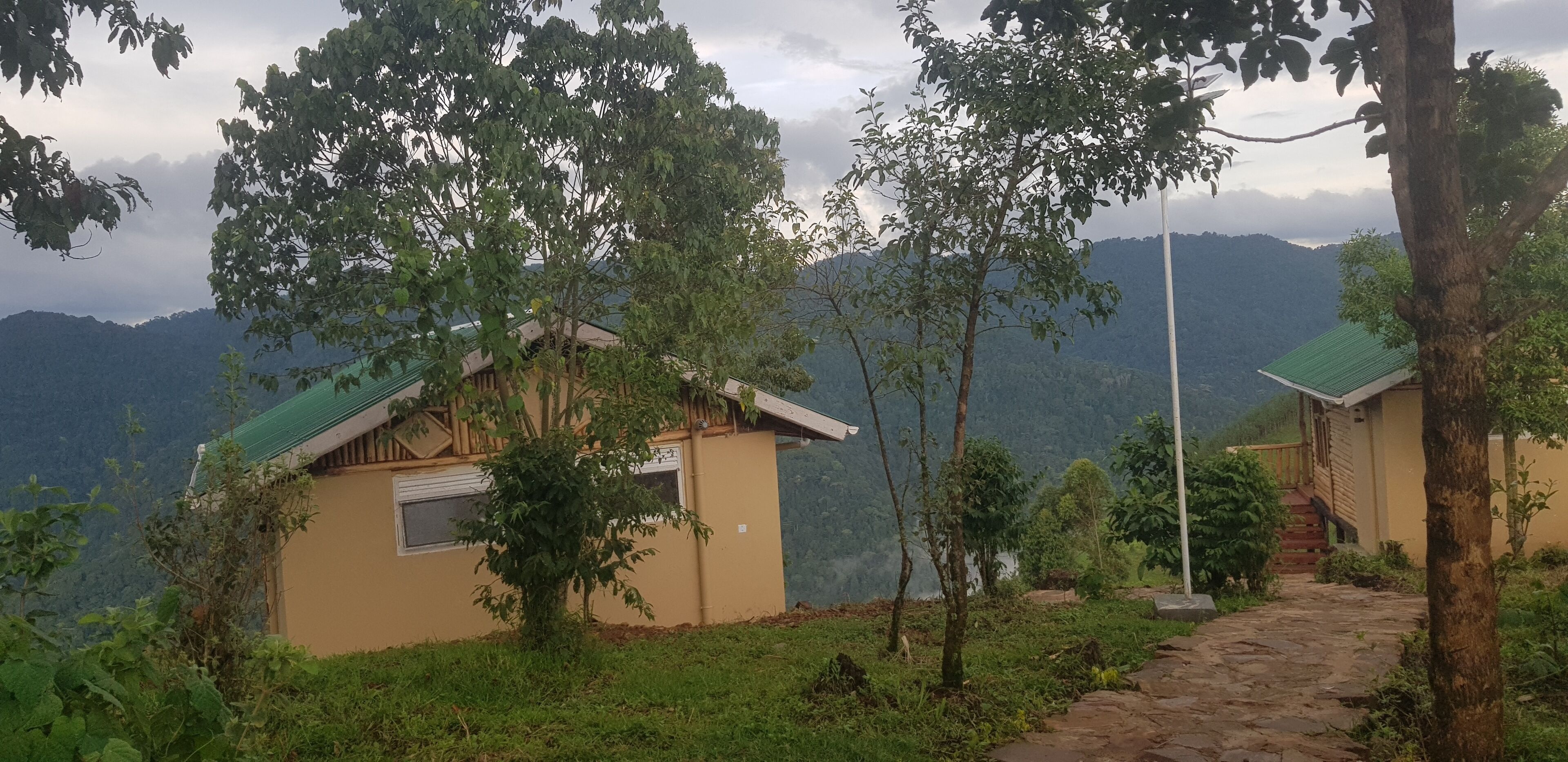 Uma cabana com telhado verde, rodeada por vegetação exuberante e um cenário montanhoso.