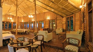A log cabin interior with wooden walls, a high ceiling, and a dining area with tables and chairs. - Orugano Bwindi Lodge (Nkuringo)