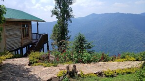 A wooden cabin with a green roof, a stone pathway, and a sign indicating 'Kanayeki'. - Orugano Bwindi Lodge (Nkuringo)
