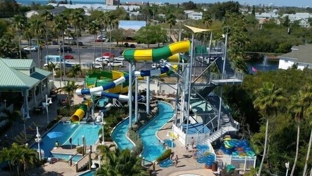 A water park with multiple pools and slides, surrounded by palm trees and lounge areas. - Gulf Coast Get-Away! Heated pool, sleeps 10! 69th (Largo)