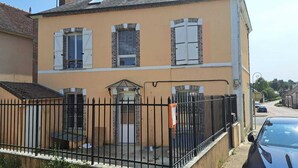 Ein zweistöckiges Gebäude mit einer beige farbenen Fassade, einem schwarzen Metallzaun und einer kleinen Terrasse.