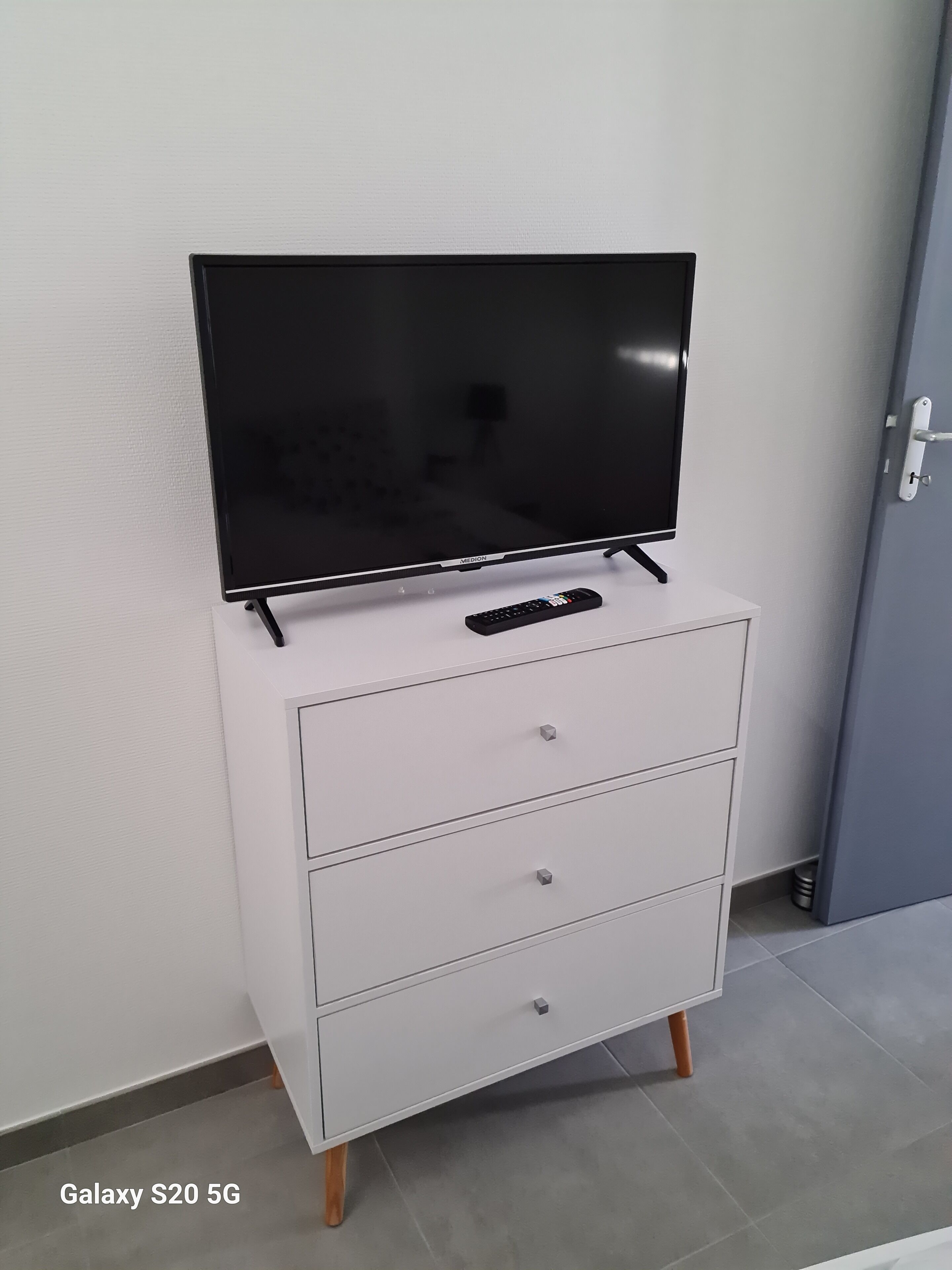 Un mobile bianco con un televisore a schermo piatto sopra, un telecomando e tre cassetti.