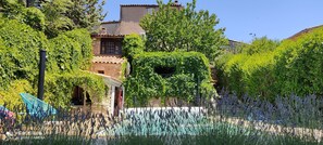 A stone building with a tiled roof, surrounded by lush greenery and lavender plants. - Large character house with private pool, View of the hills (Rustrel)