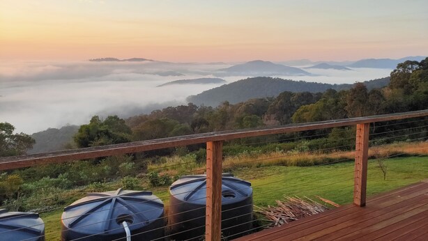 Une vue depuis une terrasse en bois donnant sur un paysage vallonné, avec une zone herbeuse et plusieurs grands réservoirs d’eau.