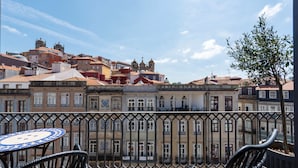A balcony with a view of historic buildings, a round table, and wicker chairs.