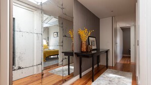 A hallway with a wooden floor, a black console table with a vase of yellow flowers, and a framed picture.