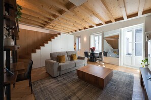 A spacious living area with a wooden ceiling, a grey sofa, a coffee table, and a staircase leading to another level.