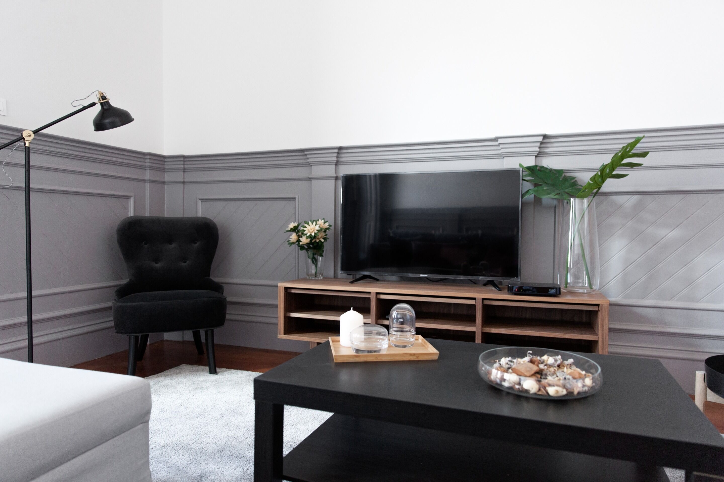Una sala de estar moderna con un sillón de cuero negro, un mueble de madera para entretenimiento con televisor de pantalla plana, una mesa de centro negra con objetos decorativos y un sofá blanco.