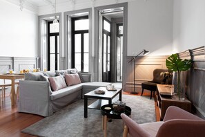 En moderne stue med en grå hjørnesofa, et lille sort sofabord og et stort vindue med naturligt lys.