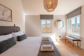 A modern bedroom with a large bed, a bench, a window with a view, and a hanging light fixture. - NEW! Prime Riverside Duplex (Porto)