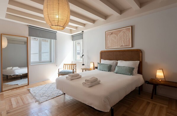 A bedroom with a large bed, a bedside table with a lamp, a chair, and a mirror.