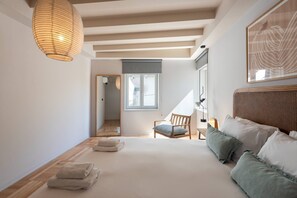 A bedroom with a large bed, a chair, a bedside table, a hanging light fixture, and a window.