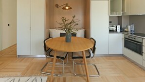 A modern kitchen with a round wooden table, chairs, a hanging light fixture, and a built-in oven. - Prime Riverside near the river (Porto)