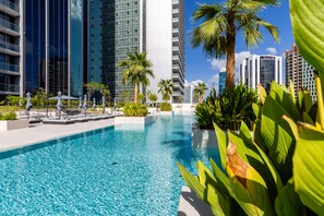 A swimming pool with lounge chairs and palm trees, surrounded by tall buildings.