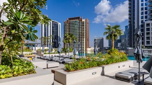 A rooftop lounge area with outdoor seating, a pool, and modern buildings in the background. -  Maison Privee - Exquisite Duplex with Private Patio & Loft Living (Dubai)
