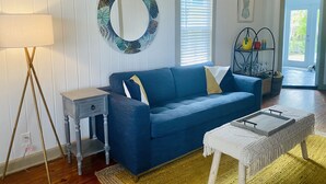 Ein Wohnzimmer mit einem blauen Sofa, einem runden Spiegel, einer Lampe und einem kleinen Tisch.