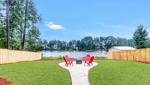 Patio trasero con un brasero, sillas Adirondack rojas y vista a un lago.