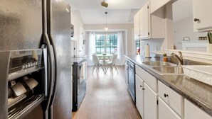 Una cocina moderna con una isla central, electrodomésticos de acero inoxidable y un área de comedor con luz natural.