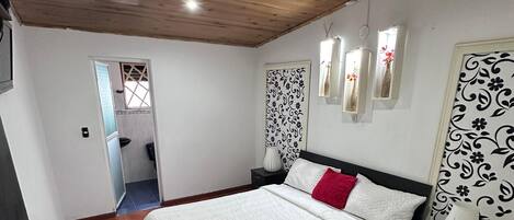 Un dormitorio con techo de madera, una cama con ropa de cama blanca, un almohárraga rojo y paneles decorativos en la pared.