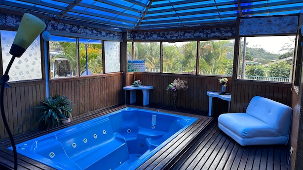 Une terrasse en bois avec un jacuzzi, un canapé blanc et une petite table sur laquelle est posé un vase de fleurs.