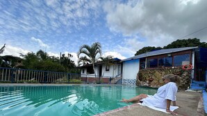 Une personne assise au bord d’une piscine, avec une maison en arrière-plan.