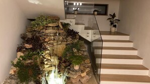 A staircase with a glass railing, a stone wall with plants, and a small waterfall feature.