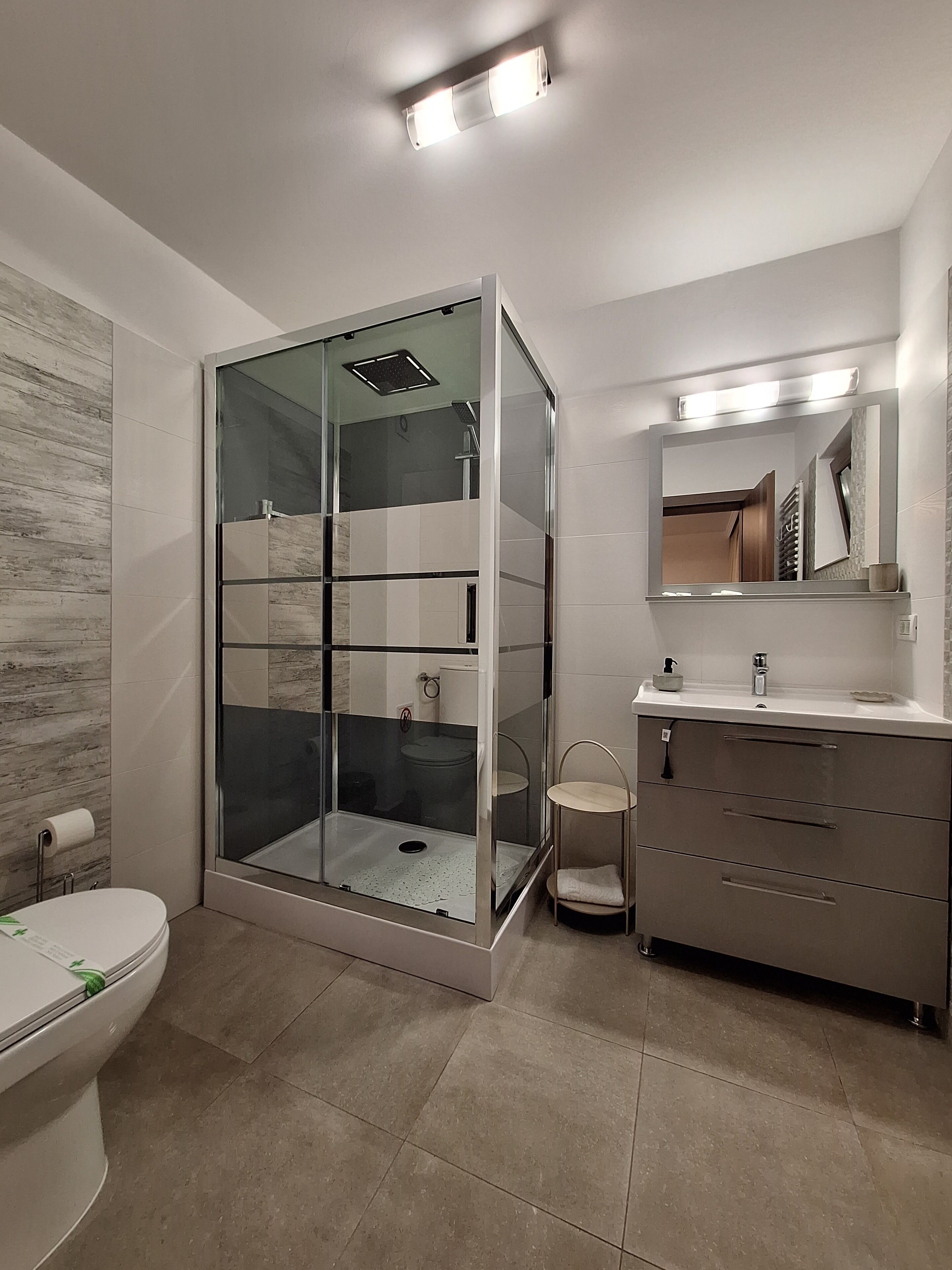 A modern bathroom with a glass-enclosed shower, a toilet, and a vanity with a mirror.