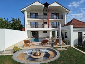 A two-story house with a swimming pool, outdoor seating, and a fire pit.