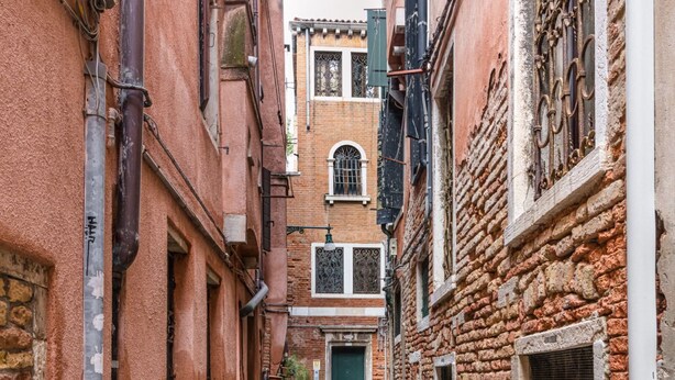 A narrow alleyway with buildings on either side, featuring a green door and a window with decorative ironwork. - The Silk House - Travel Sustainable (Venezia)