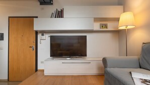 A modern kitchen with a built-in oven, a microwave, and a small refrigerator. There is a wooden door and a grey sofa in the living area. - The Silk House - Travel Sustainable (Venezia)