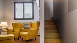 A modern living room with yellow armchairs and a wooden floor, a staircase with wooden steps, and a window with blinds. - The Silk House - Travel Sustainable (Venezia)