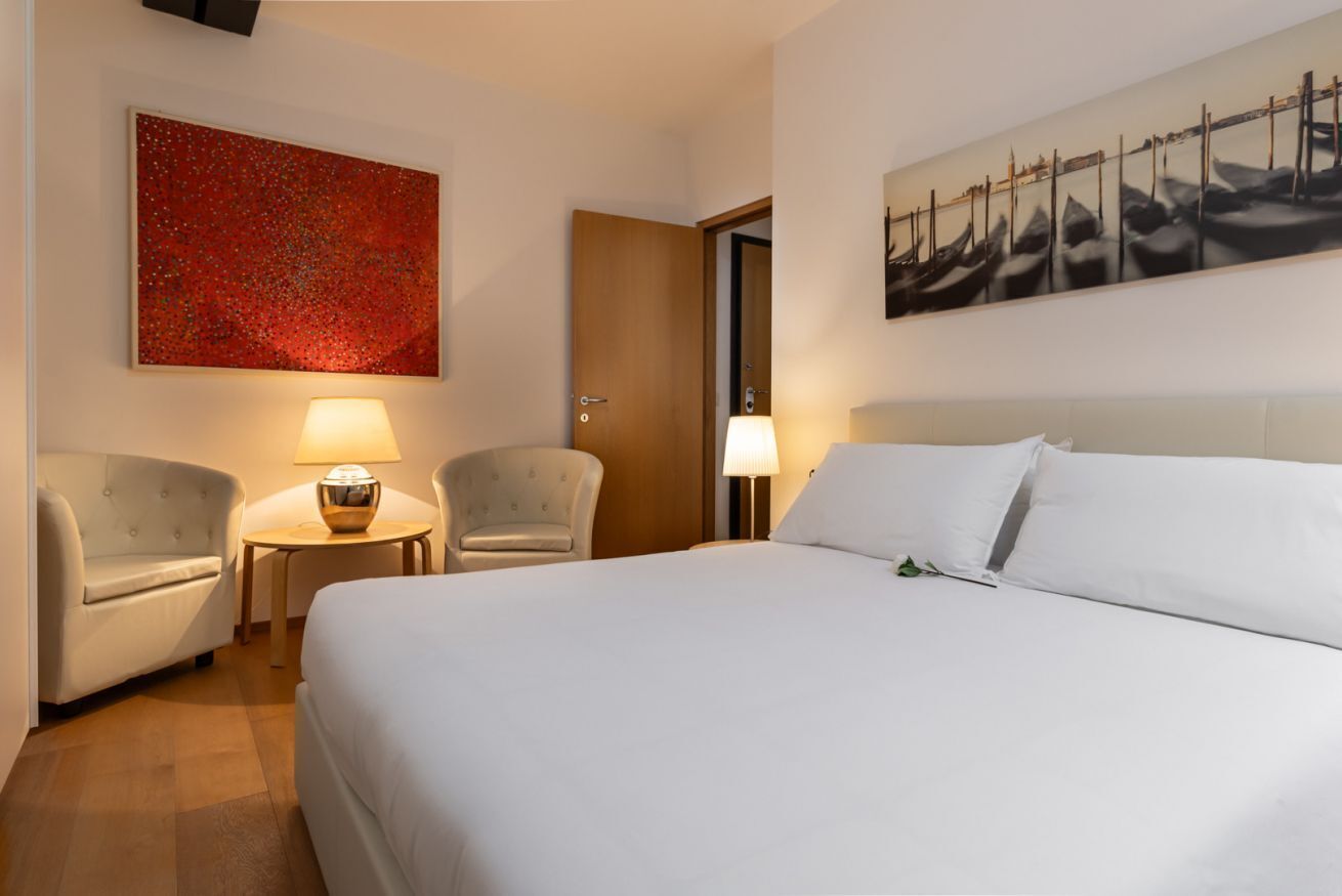 Ett hotellrum med en stor säng, två fåtöljer, ett litet bord och två lampor.