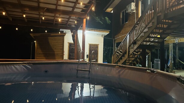 En swimmingpool med en træterrasse, en trappe og en bygning med dør og vinduer.