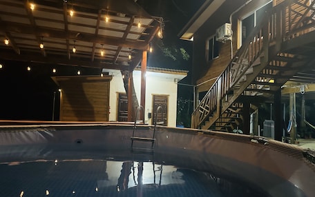 A swimming pool with a wooden deck, a staircase, and a building with a door and windows.