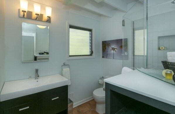 A bathroom with a white sink, dark cabinets, a glass shower enclosure, and a toilet.