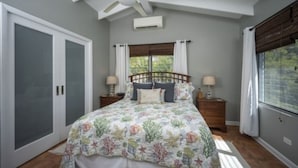 A bedroom with a bed, a ceiling fan, a window with curtains, and a nightstand with a lamp.
