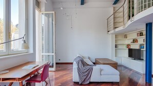 Una sala de estar moderna con suelo de madera, un sofá blanco, una mesa de comedor con sillas y un televisor sobre un mueble blanco.