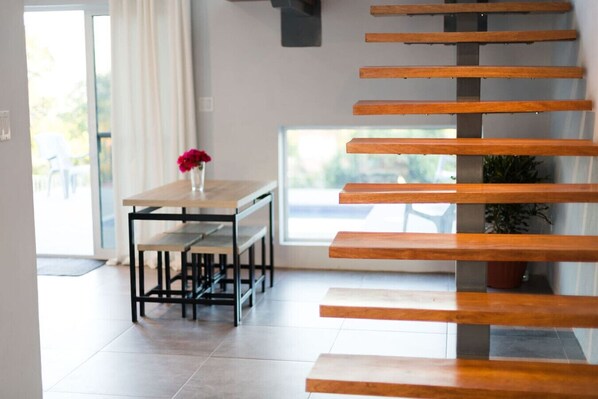 A modern interior with a wooden staircase, a dining table with benches, and a potted plant.