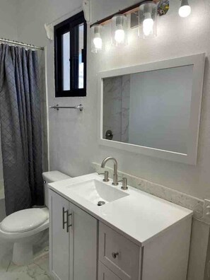 Une salle de bain avec un lavabo blanc, un miroir et une fenêtre au-dessus du lavabo.