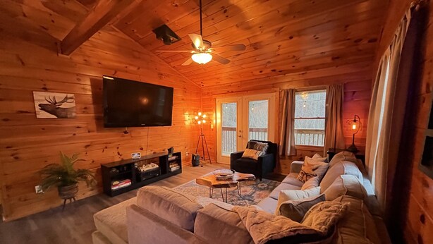 A cozy log cabin interior with a large sectional sofa, a flat-screen TV, and a ceiling fan.