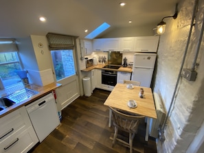 A compact kitchen with white cabinets, a wooden countertop, a built-in oven, and a window with a view of the garden. - 400 year old Grade II listed stone cottage, Pilton; Glastonbury
AA 4* Gold Award (Pilton)