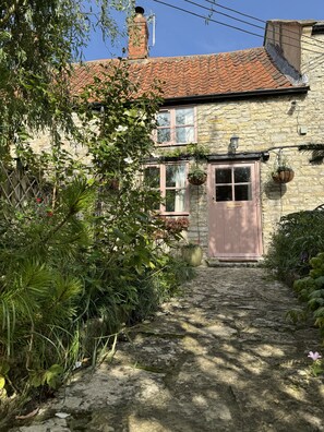 A stone house with a tiled roof, a wooden door, and a cobblestone path leading to it. - 400 year old Grade II listed stone cottage, Pilton; Glastonbury
AA 4* Gold Award (Pilton)