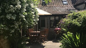 A garden area with a patio table and chairs, surrounded by lush greenery and flowering plants. - 400 year old Grade II listed stone cottage, Pilton; Glastonbury
AA 4* Gold Award (Pilton)