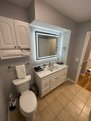 Une salle de bain comprenant des toilettes, un lavabo, un meuble-lavabo et un miroir doté d’un éclairage intégré.