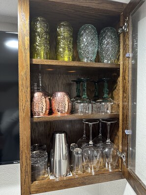 Un meuble en bois doté d’étagères contenant divers objets en verre, notamment des bouteilles, des verres et des gobelets.